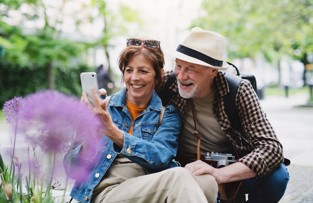 Older couple outdoors taking photos with their phone.